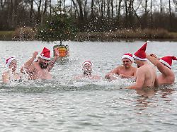 07 12 2025 baden wuerttemberg ertingen maenner und eine frau mit nikolausmuetzen baden bei einstelligen temperaturen im schwarzachtalsee im hintergrund schwimmt ein weihnachtsbaum auf einer boje