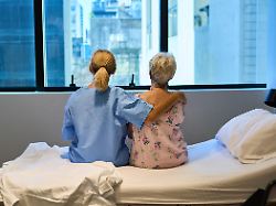 a nurse sits comforting an elderly woman in a hospital room during the daytime the photo conveys care support and professional medical assistance in a serene healthcare environment