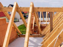 auf dem neubau von einem wohnhaus wird mit dachbalken ein neuer dachstuhl montiert als symbolbild fuer wohnbau und wohnungspolitik