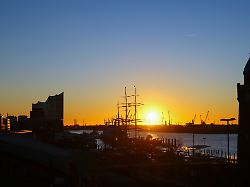 blick bei sonnenaufgang ueber die landungsbruecken im hafen im hintergrund ist die markante silhouette der elbphilharmonie l zu sehen
