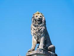 der bayerische loewe an der hafeneinfahrt von lindau am bodensee steinerne statue auf hohem sockel vor blauem himmel