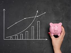 die hand einer frau haelt eine rosa keramikschweinbank vor einem kreideboard hintergrund mit einem wachsenden graph und einem balkendiagramm in kreide gezogen