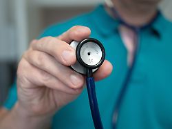 ein hausarzt steht in seiner hausarztpraxis und haelt ein stethoskop