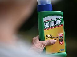eine frau haelt in ihrem garten eine flasche des unkrautvernichters roundup mit dem wirkstoff glyphosat von bayer in der hand gestellte szene