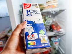 eine hand haelt eine h vollmilch vor dem geoeffneten kuehlschrank