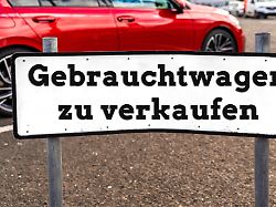 fotomontage ein schild mit der aufschrift gebrauchtwagen zu verkaufen steht auf einem parkplatz vor einem roten auto