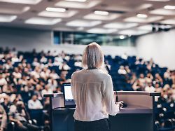 female speaker giving a talk on corporate business conference unrecognizable people in audience at conference hall