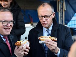 german chancellor friedrich merz and thuringia s state premier mario voigt each hold a sausage in a bun during merz s visit to a school in jena lobeda in thuringia germany december 2 2025 1