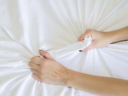 hand zeichen orgasmus der frau auf weissem bett hand der weiblichen ziehen weissen laken in ekstase gefuehl und emotion konzept