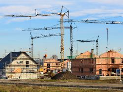 in einem neubaugebiet stehen viele baukraene vor wohnhaeuser im rohbau als symbolbild fuer wohnbau und wohnungspolitik digital bearbeitet