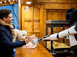 max nimmt vom humanoiden roboter optimus von tesla bei dessen vorstellung in der mall of berlin popcorn an einem weihnachtsmarktstand entgegen