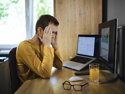 ein mann mittleren alters sitzt an einem holzschreibtisch und haelt sich frustriert den kopf