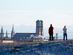 ein mann und eine frau nutzen das schoene wetter im olympiapark fuer einen spaziergang im hintergrund sind die tuerme des rathauses l r der kirche alter peter und der frauenkirche zu sehen