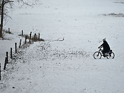 ein radfahrer faehrt in der naehe des uracher wasserfalls am rand der schwaebischen alb ueber eine schneebedeckte wiese
