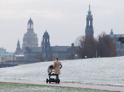 eine frau geht am 22 01 2018 in dresden sachsen mit einem kinderwagen vor der kulisse der dresdner altstadt an den verschneiten elbwiesen entlang