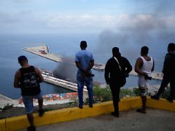 maenner beobachten wie rauch von einem dock aufsteigt nachdem im hafen von la guaira venezuela am samstag 3 januar 2026 explosionen zu hoeren waren