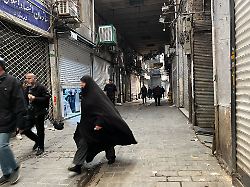 menschen gehen in teherans jahrhundertealtem hauptbasar an geschlossenen geschaeften vorbei