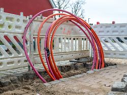 schleswig ein dicker strang teils aufgerolltes glasfaserkabel bereit um verlegt zu werden in einem ausgehobenen loch einer baustelle hier wird glasfaser verlegt um fuer schnelleres internet zu sorgen