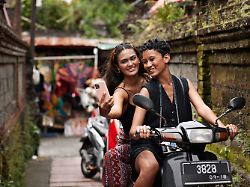 smiling female friends taking selfie during scooter ride at vacation