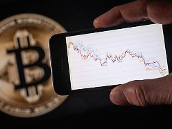 this illustration photograph shows a man holding a phone with a downward trend in the stock market in front of a screen displaying a bitcoin logo in mulhouse on december 5 2025