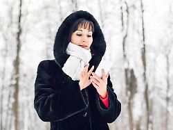young woman smiling with smart phone and winter landscape young woman smiling with smart phone and winter landscape and snowflakes on the background model released 97797392