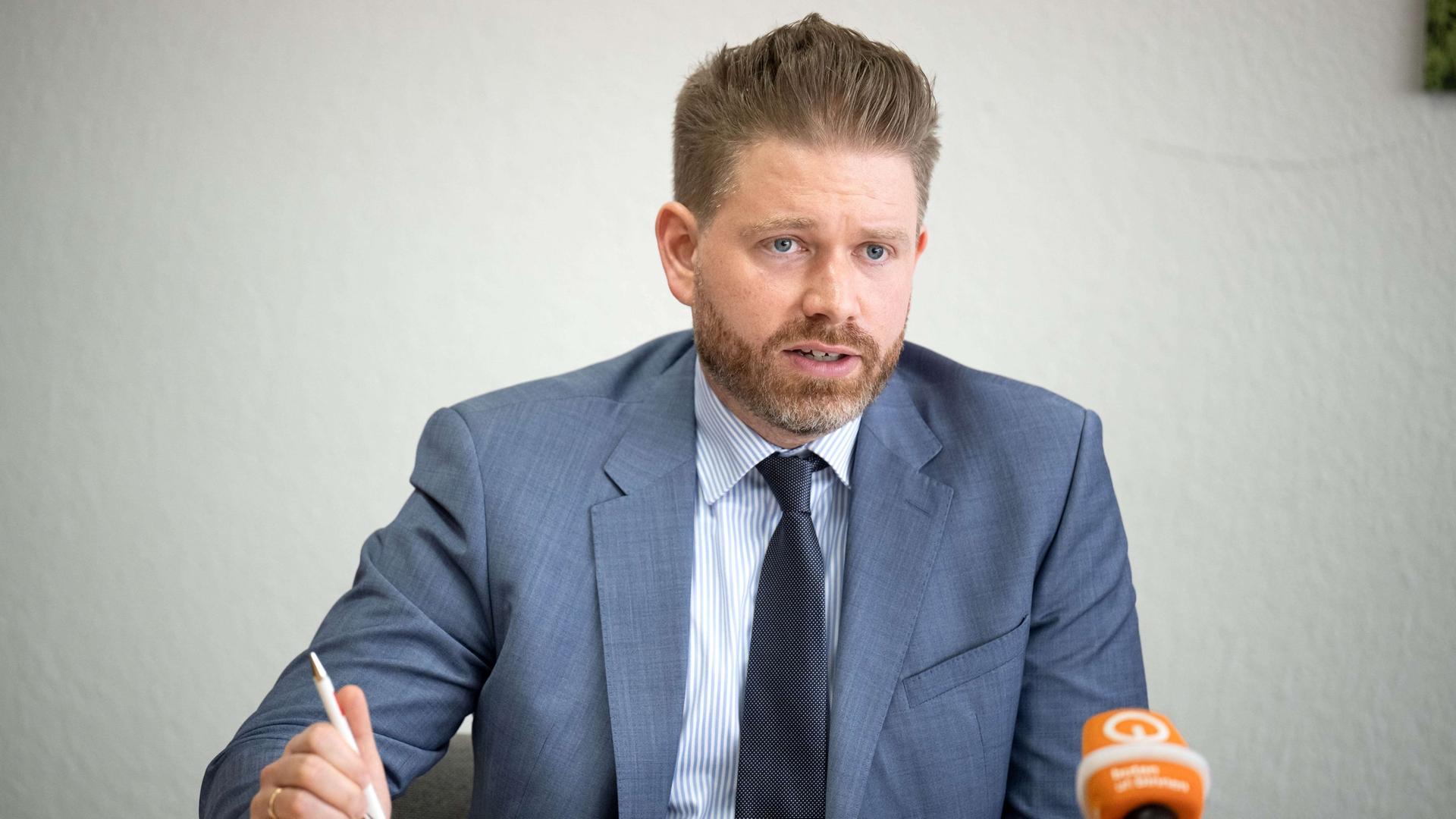 rb thorge koehler sitzt in anzug an einem tisch und spricht in einen butenunbinnen mikrofon 100