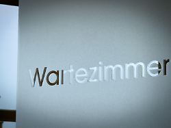 a sleek waiting room entrance features a brushed metal wartezimmer sign on a frosted glass panel