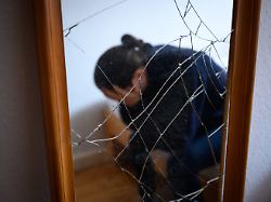 archiv 11 02 2023 hamburg illustration eine frau sitzt neben einem gesprungenen spiegel auf einem bett und haelt ihren kopf in den haenden dabei ist ihr abbild im spiegel zu sehen gestellte szene