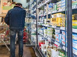 ein kunde steht in einem supermarkt vor dem kuehlregal mit milchprodukten