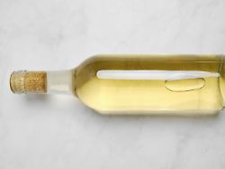 eine glasflasche mit weisswein auf einer glatten hellen oberflaeche die flasche hat einen korkdeckel und zeigt die fluessigkeit im inneren die klar und hell erscheint