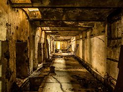 langer korridor in einem verlassenen industrigebaeude wechselt sich mit licht und schatten ab und gibt starke kontraste in brauntoenen ganz gerade und symmetrisch zum fluchtpunkt hin