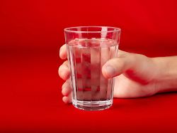 male hand holding a glass cup with water inside isolated on red background