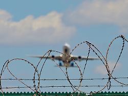symbolbild abschiebeflug ein startendes flugzeug hinter einem stacheldrahtzaun