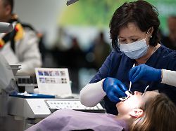 symbolfoto fueur zahnaerztin mit schutzmaske und behandelt eine patientin die patientin liegt entspannt auf einem rosa behandlungsstuhl waehrend die zahnaerztin mit professionellem equipment arbeitet