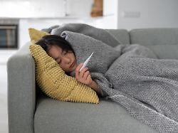 winter illnesses young sick unhealthy asian woman suffering from fever measuring temperature with thermometer while lying under blanket on sofa at home
