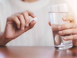 woman s hand taking medicine pill and drinking water with the brown bottle on the table for healthcare concept