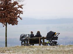zwei frauen mit kinderwagen sitzen auf einer bank waehrend hochnebel ueber oberschwaben haengt