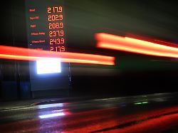 autos fahren am fruehen morgen im regen an der anzeigetafel einer tankstelle vorbei auf der benzin und dieselpreise zu sehen sind