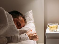 der kranke mann schlaeft mit einer decke bedeckt die im bett mit hohem fieber liegt und im wohnzimmer ruht er ist erschoepft und leidet an grippe mit tasse tee mit zitrone medikamente influenza saison