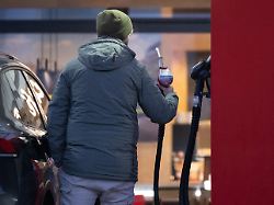 ein mann haelt an einer tankstelle eine zapfpistole