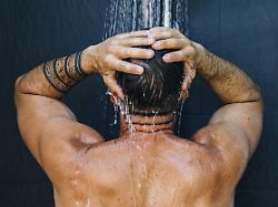 ein mann mit tattoos geniesst eine erfrischende dusche und steht mit dem ruecken zur kamera