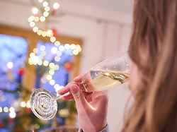 ein teenager trinkt ein glas sekt waehrend ein weihnachtsbaum im hintergrund leuchtet