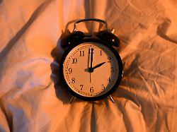 ein wecker liegt im daemmrigen licht auf einer bettdecke am 29 03 2026 beginnt die sommerzeit in deutschland