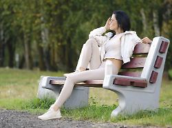 eine frau sitzt auf einer parkbank bekleidet mit leichter sportkleidung und geniesst den warmen tag