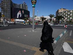 eine frau ueberquert einen fast menschenleeren platz mit einer plakatwand im hintergrund die ein portraet des getoeteten iranischen obersten fuehrers chamenei zeigt