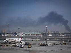 eine rauchwolke verursacht durch einen iranischen angriff ist im hintergrund zu sehen waehrend flugzeuge der emirates nach der schliessung des flughafens auf dem dubai international airport geparkt sind