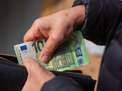 eine seniorin steckt euro banknoten in eine geldboerse