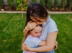mother comforting upset girl with a hug outdoors on grass model released symbolfoto property released mdof03017