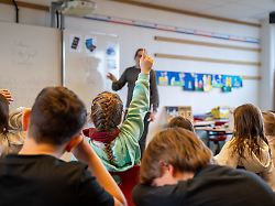 symbolbild schuelerin meldet sich im unterricht 12 02 2026 ein maedchen sitzt im klassenraum einer grundschule und hebt den arm um sich aktiv am unterricht zu beteiligen