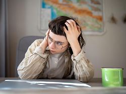 tired teen girl in glasses high school student worried about exams sitting at desk at home girl holds head after sleepless night drinks coffee tries awake insomnia lack of sleep depressed mood